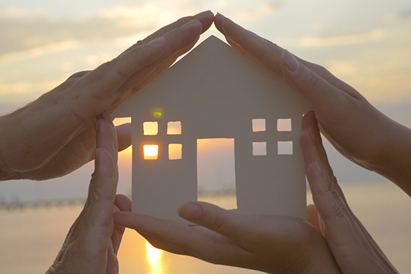 People holding house model on a beach at sunset